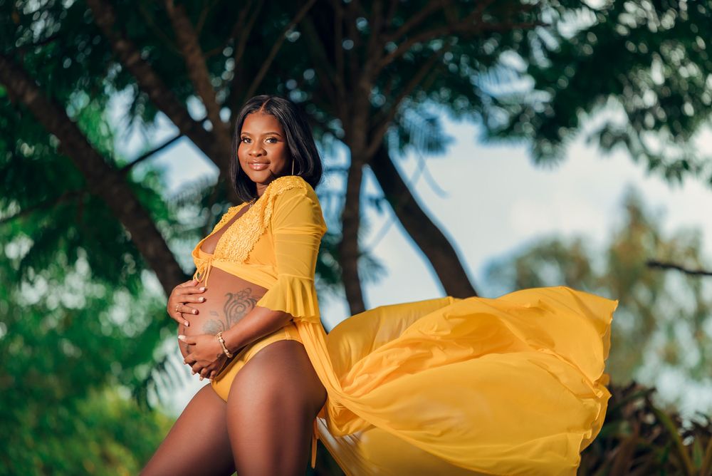Expecting mother in flowing yellow dress poses outdoors during sunset.