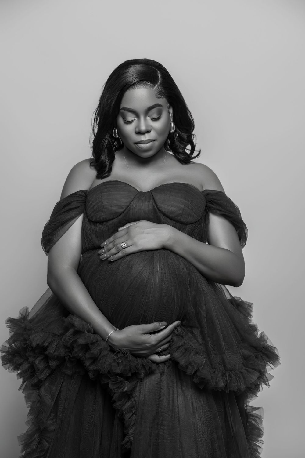 Elegant black and white maternity portrait featuring an off-shoulder gown with ruffled tulle details.