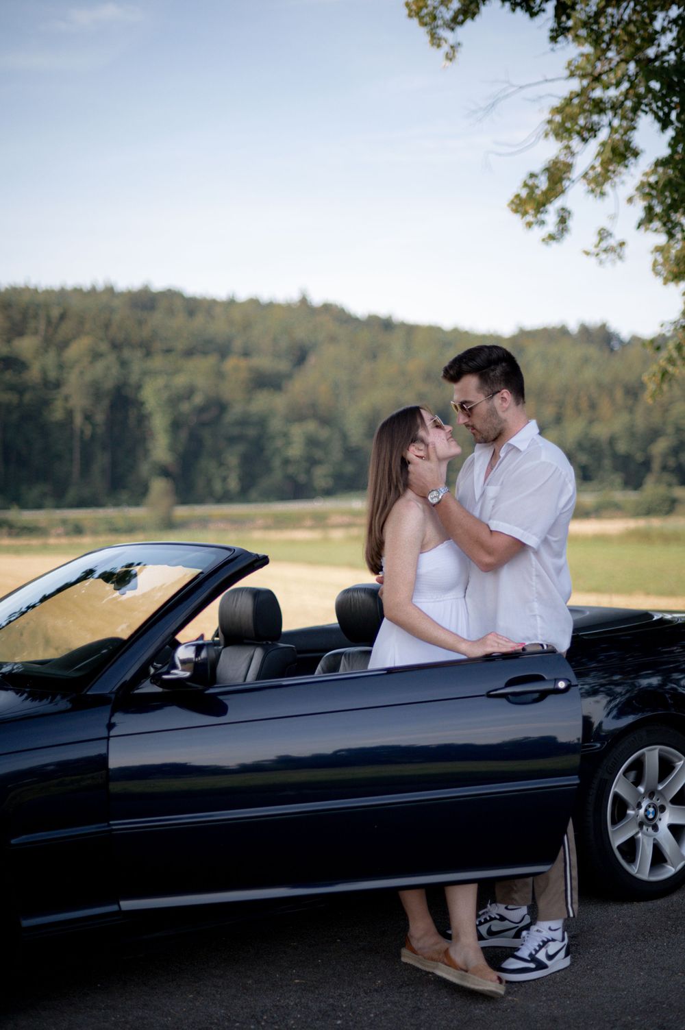 Ein junges Paar küsst sich vor einem BMW Cabrio.