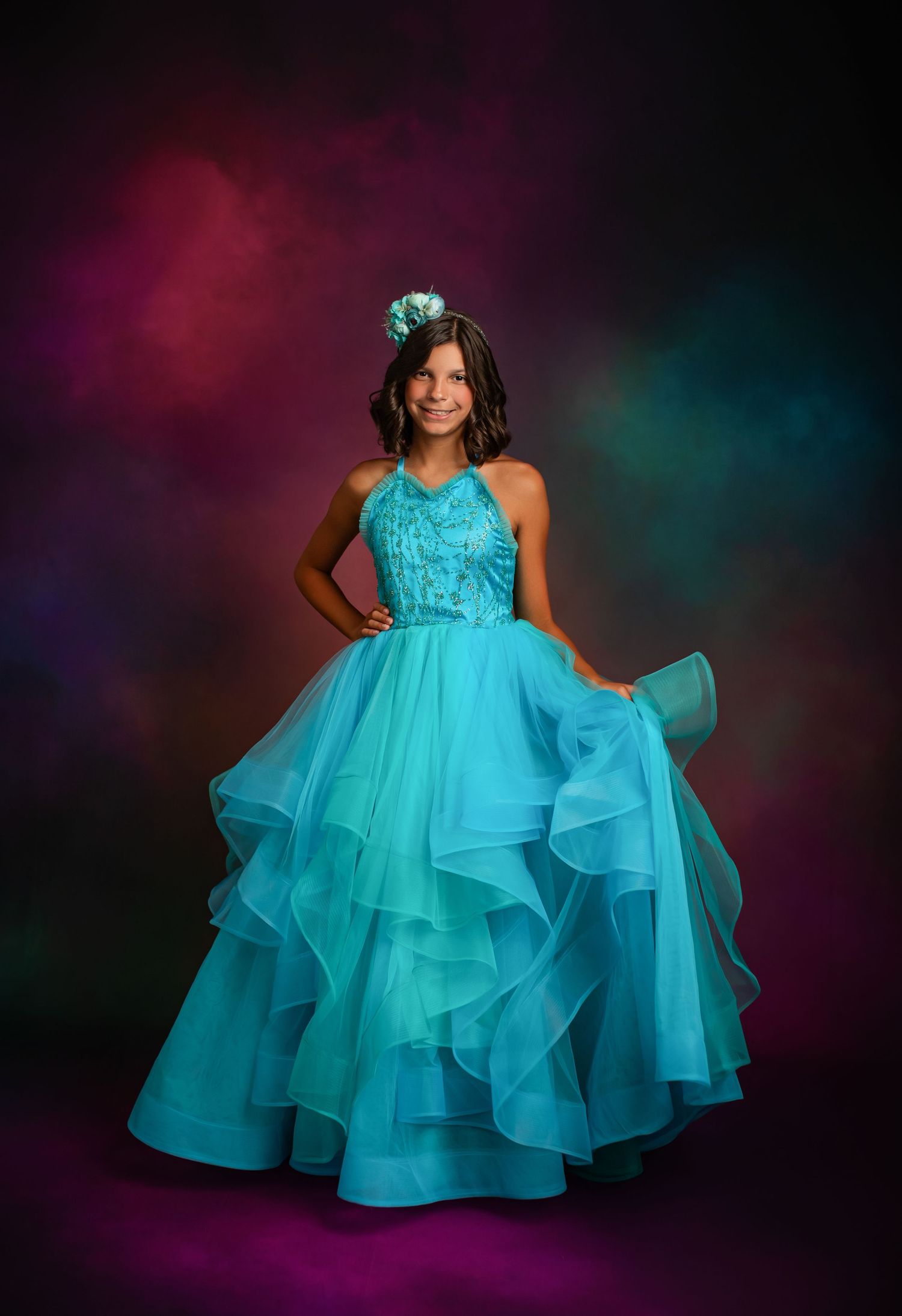 A vibrant teal ballgown dress with a full gathered skirt is shown against a warm autumn background.