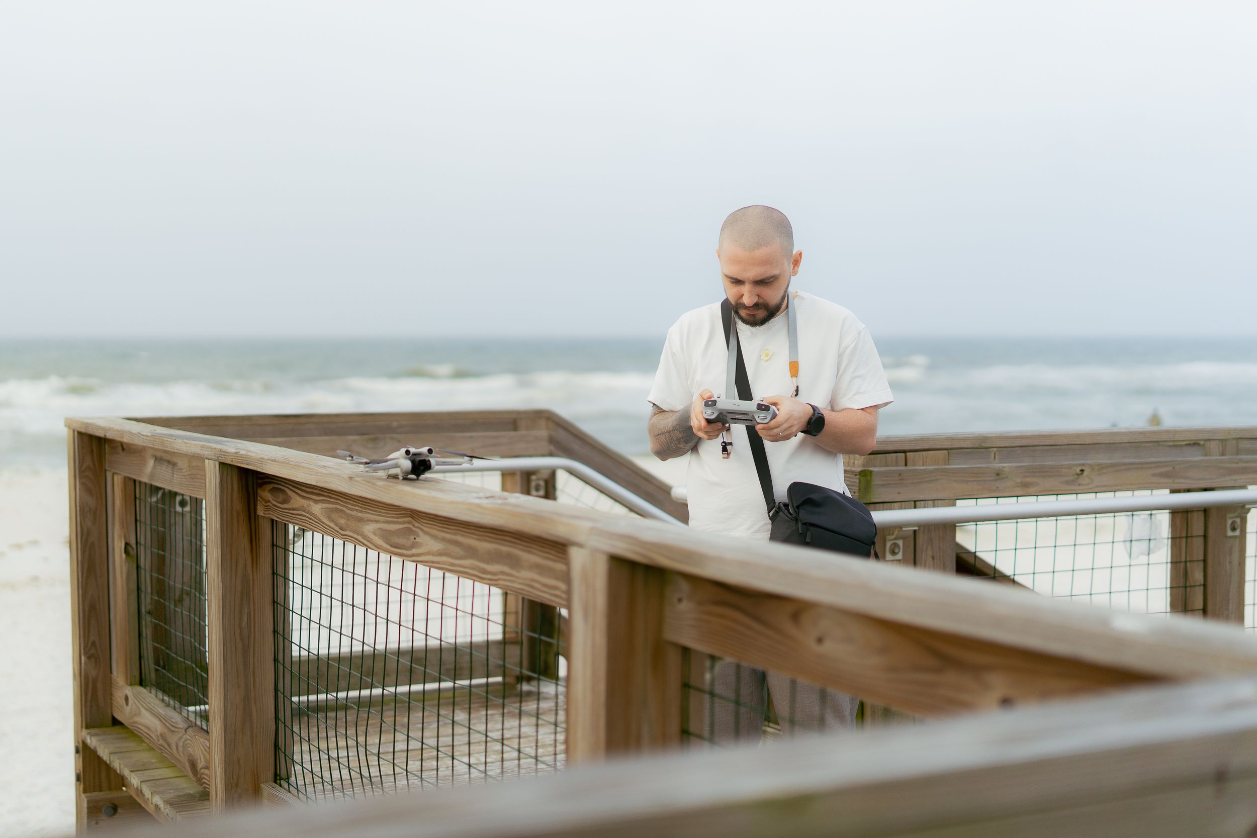 A person in a white shirt looking down at a phone while standing on a wooden oceanfront deck on a cloudy day.