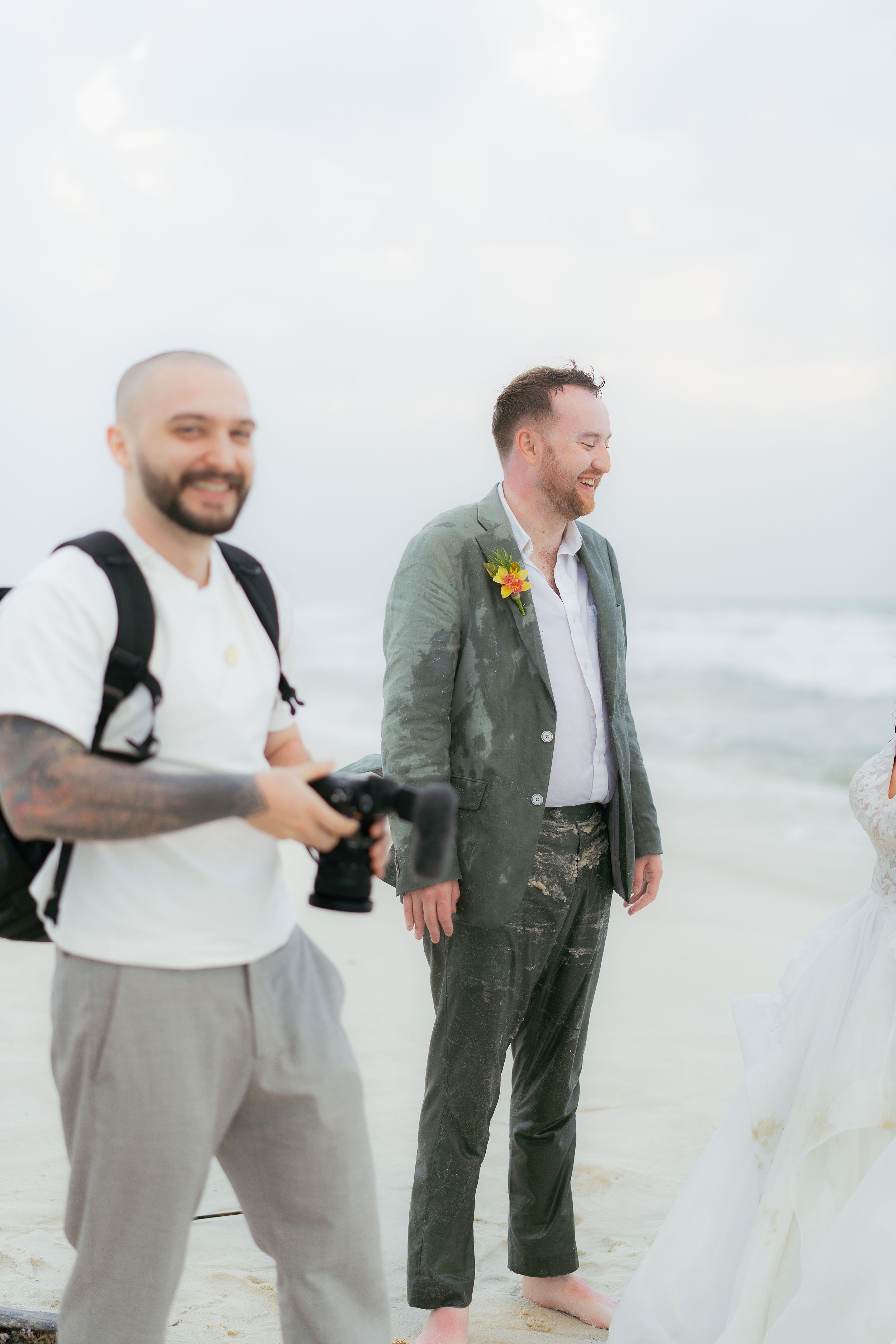 Two people enjoying a candid moment on a beach with one wearing a green suit and another in casual attire.