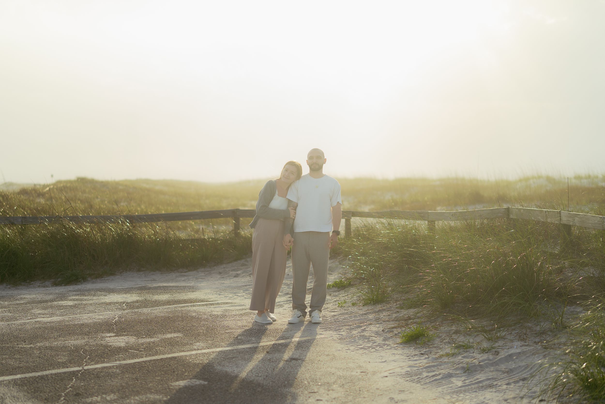 Two people walking hand in hand on a path at sunset with golden sunlight streaming through the tall grass.
