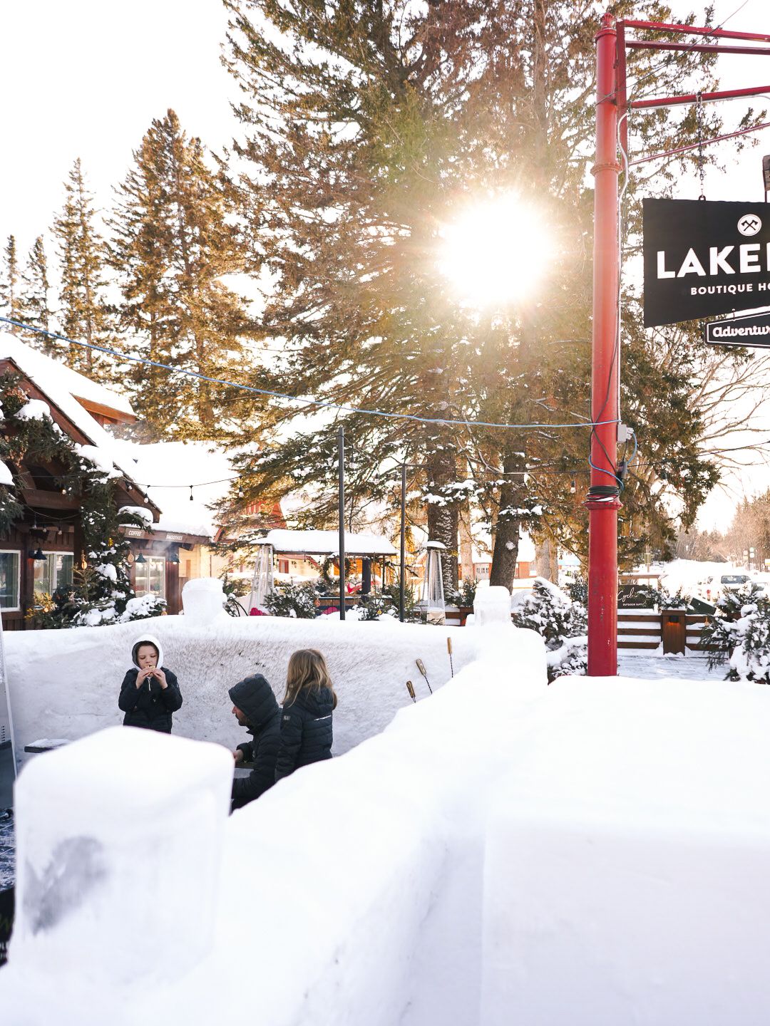 Snowy winter landscape at a ski resort with sun setting behind pine trees.