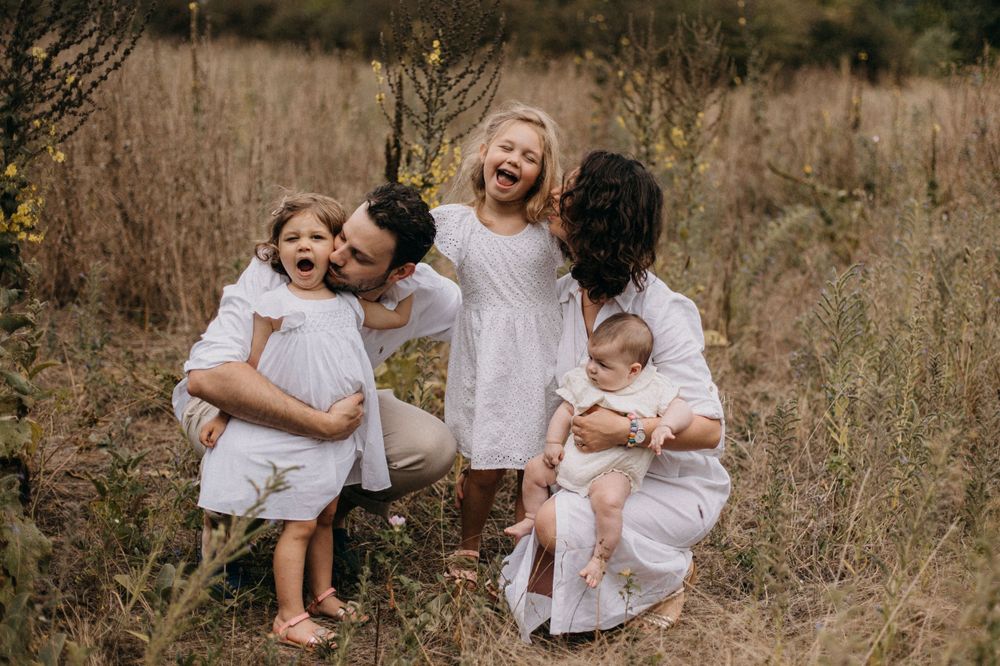 Playful family moment captured with parents and children laughing together in a field.