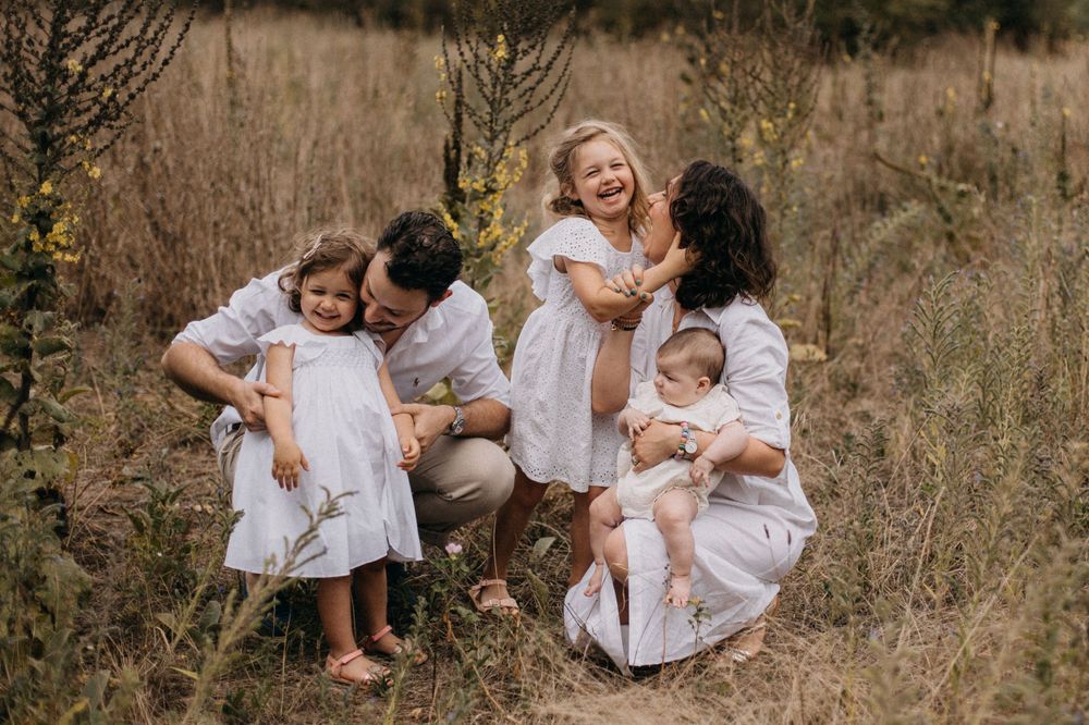 Intimate family photo showing parents and children sharing laughs while sitting in tall grass.