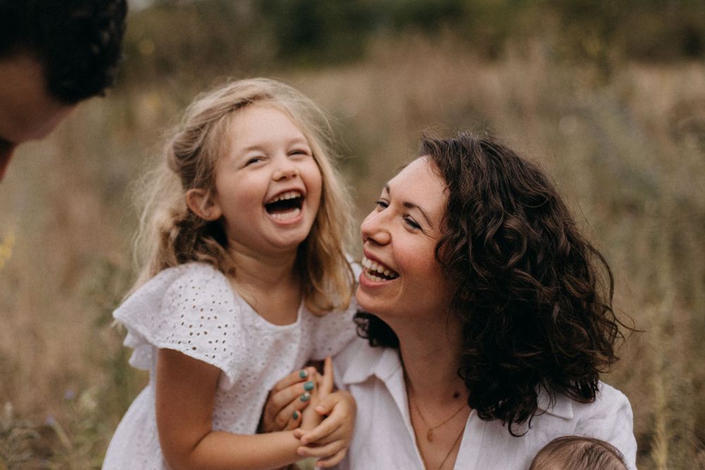 Candid portrait of parent and child laughing together against natural outdoor background.