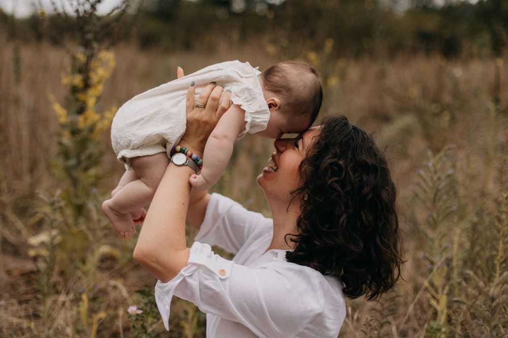 Joyful interaction between adult and baby in white clothing while standing in a golden field at sunset.
