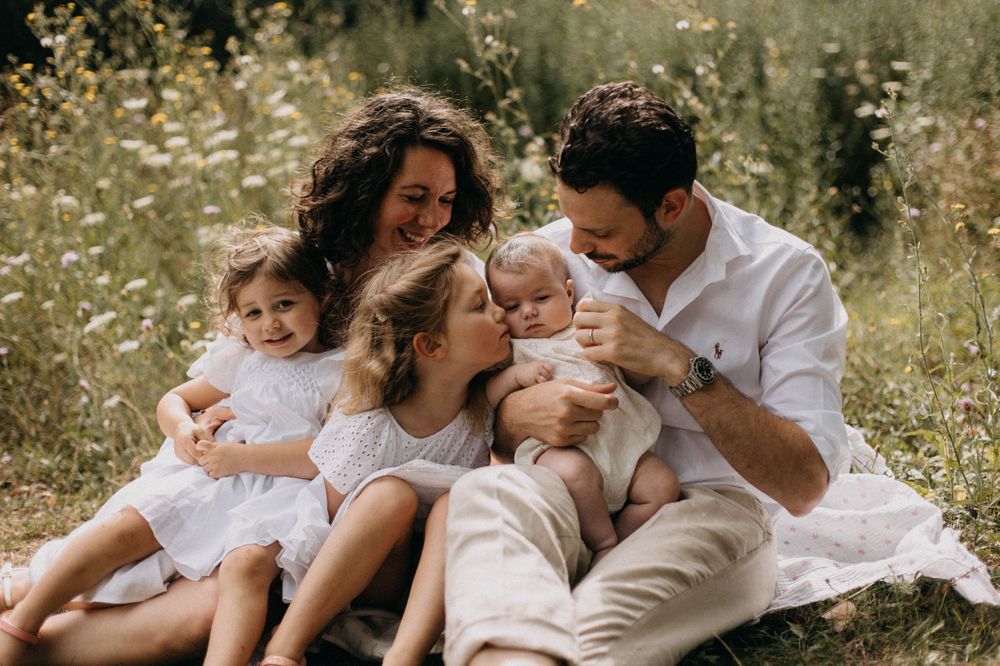 Family dressed in white sits together on blanket in wildflower meadow during golden hour photoshoot.