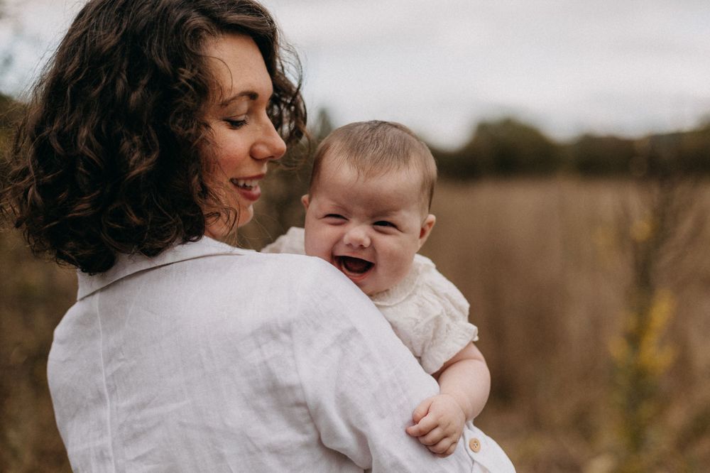 Joyful moment between adult and laughing baby captured against natural outdoor backdrop.