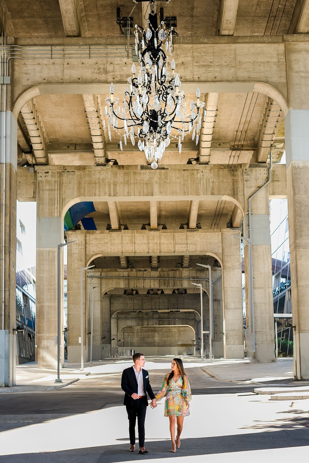 A man and a woman hold hands and walk together by the giant spinning chandelier, underneath the Granville Street Bridge in Vancouver.