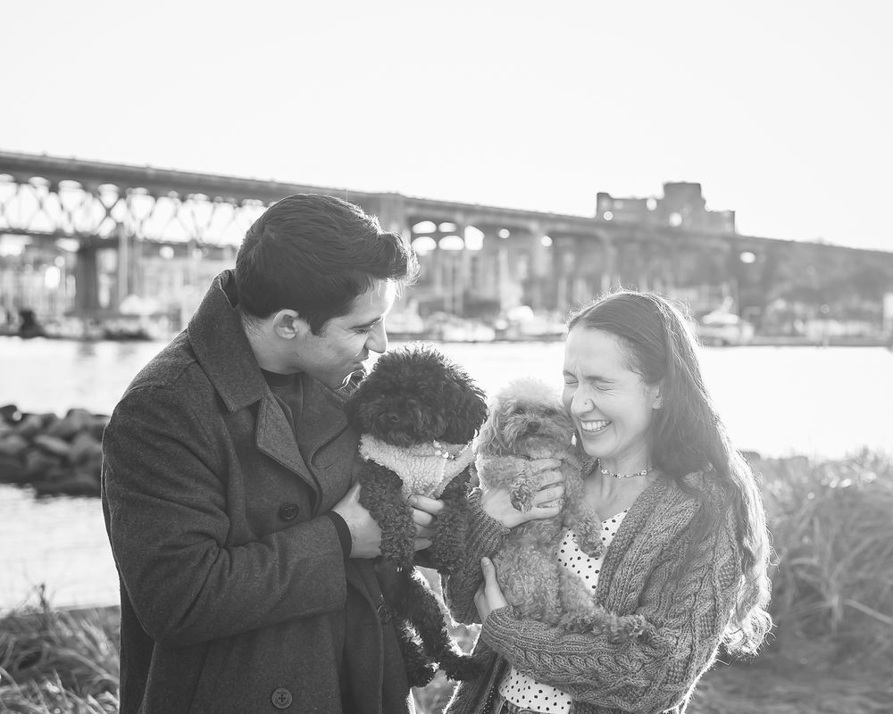 A couple includes their two dogs in their engagement session in Vancouver. A sunny day on the beach with the Burrard Street bridge behind.