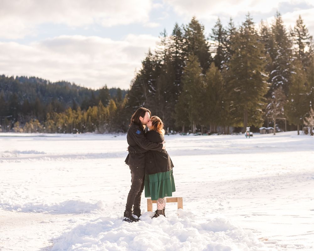 On the snowy dock of Whonnock Lake, with the frozen lake in the background, a couple embraces each other for a cozy kiss.