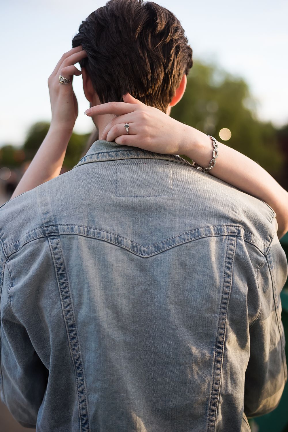A woman wraps her arms around her fiance's neck and lovingly plays with his hair.