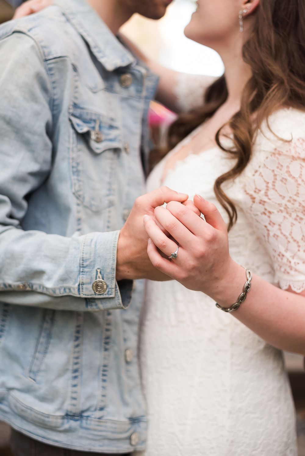 A close up photo of a couple embracing and holding hands to show a beautiful moss agate engagement ring.
