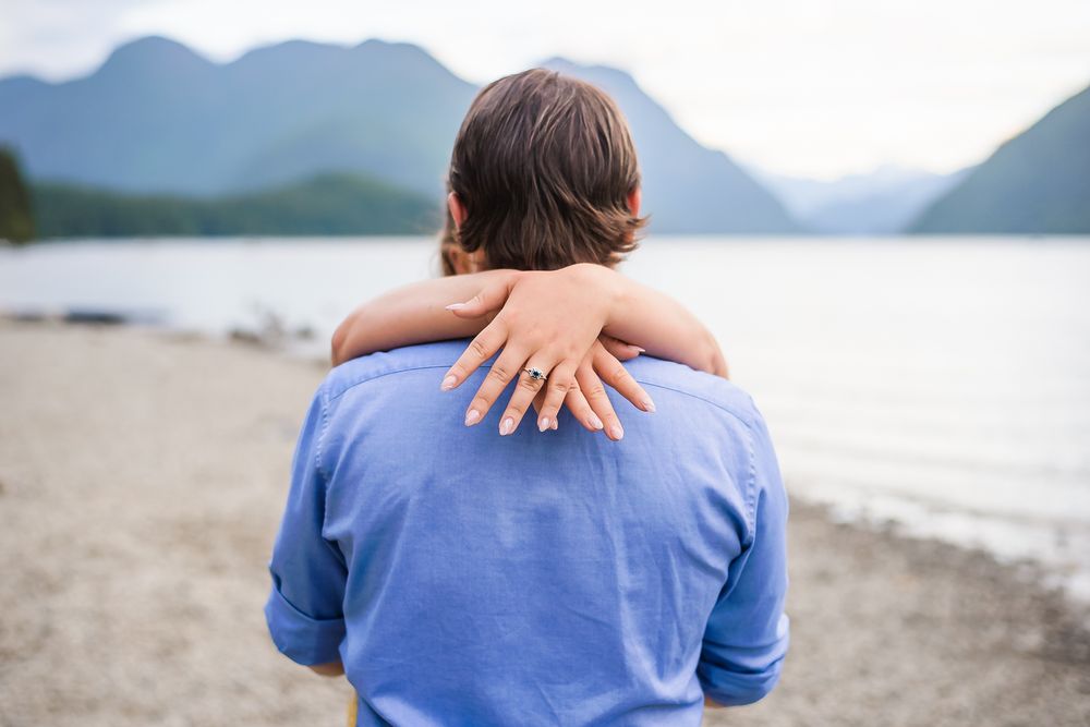 With the stunning mountains in the background, a woman wraps her arms around her fiance's neck and shows off her beautiful engagement ring.