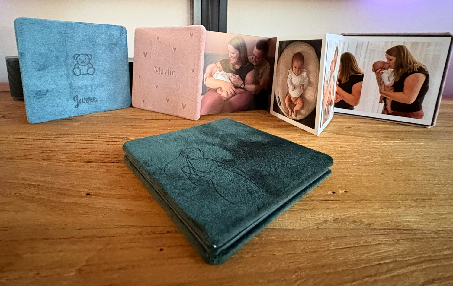 Een verzameling fluwelen fotoalbums in turquoise, roze en blauw, open uitgestald op een houten tafel, toont familiefoto's.