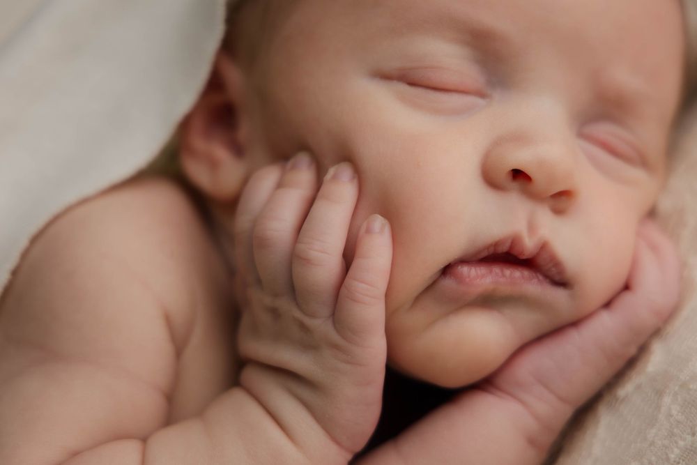 Close-up of sleeping newborn baby with tiny hands resting on cheeks.