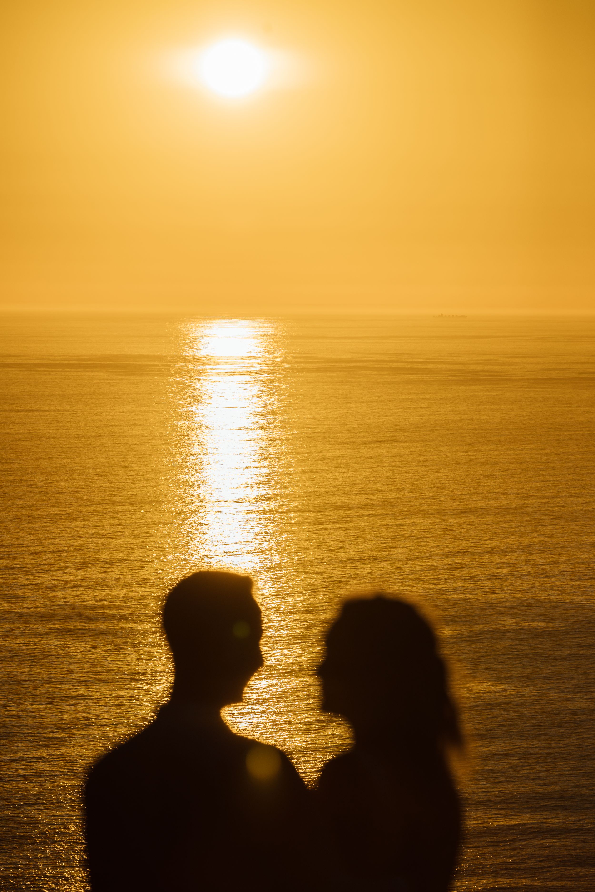 Silhouette of a romantic couple facing each other against a golden ocean sunset backdrop.