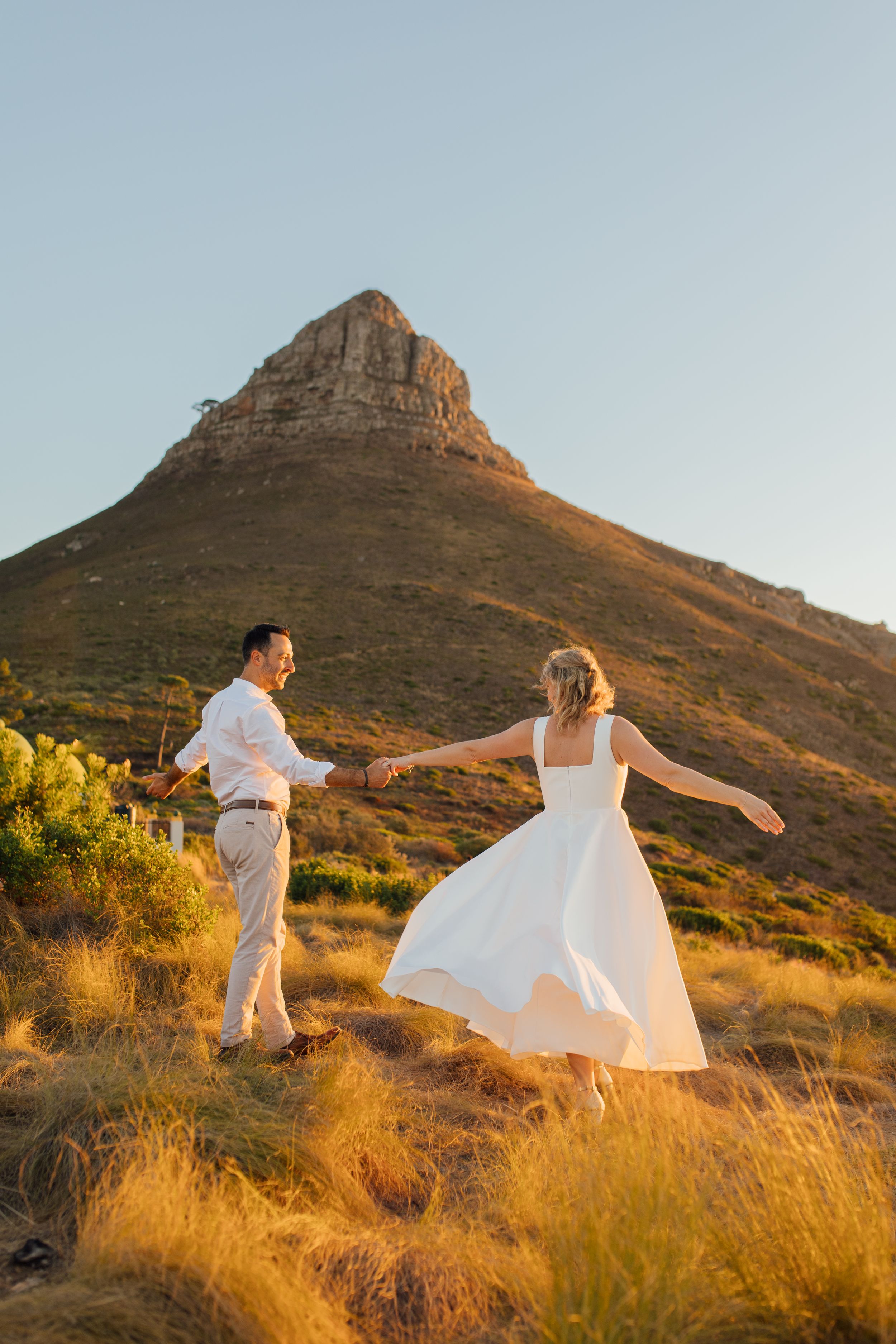 Bride and groom dancing on golden hillside with Lion's Head mountain backdrop in Cape Town at sunset.