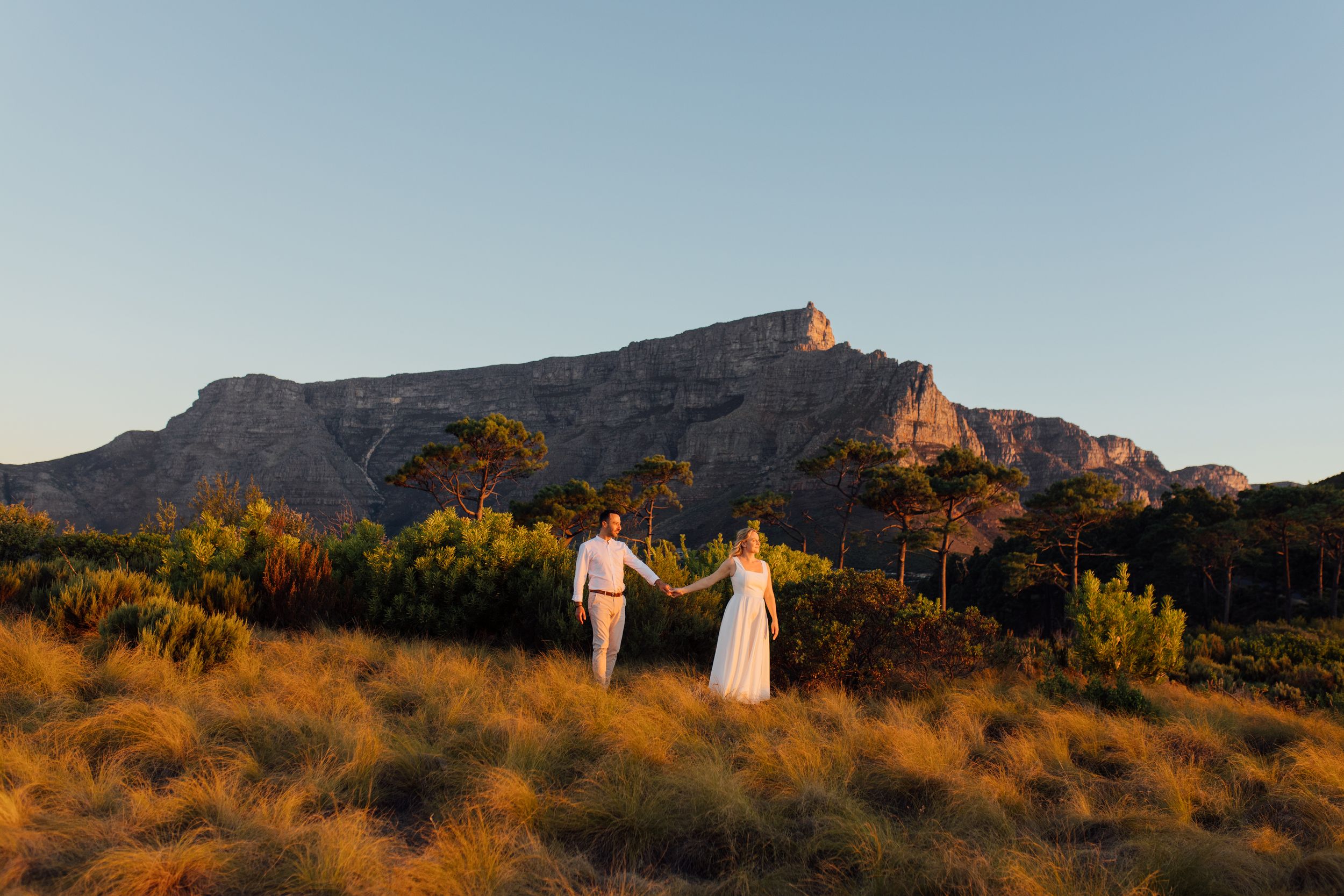 Couple holding hands at golden hour with Table Mountain backdrop in Cape Town, South Africa.