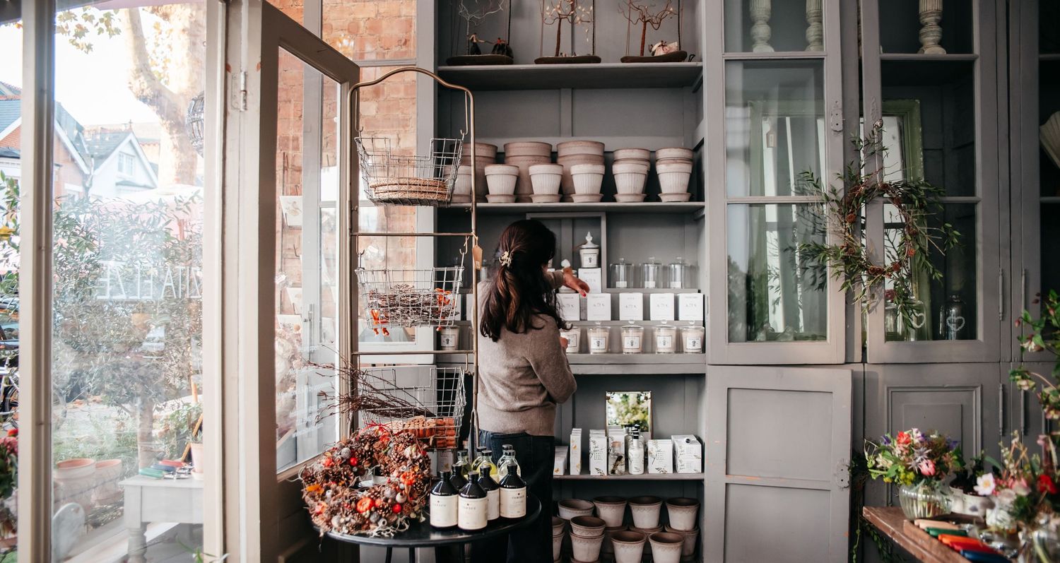 Modern bar interior with glass shelving displaying bottles and glassware against a rustic brick wall in soft lighting.
