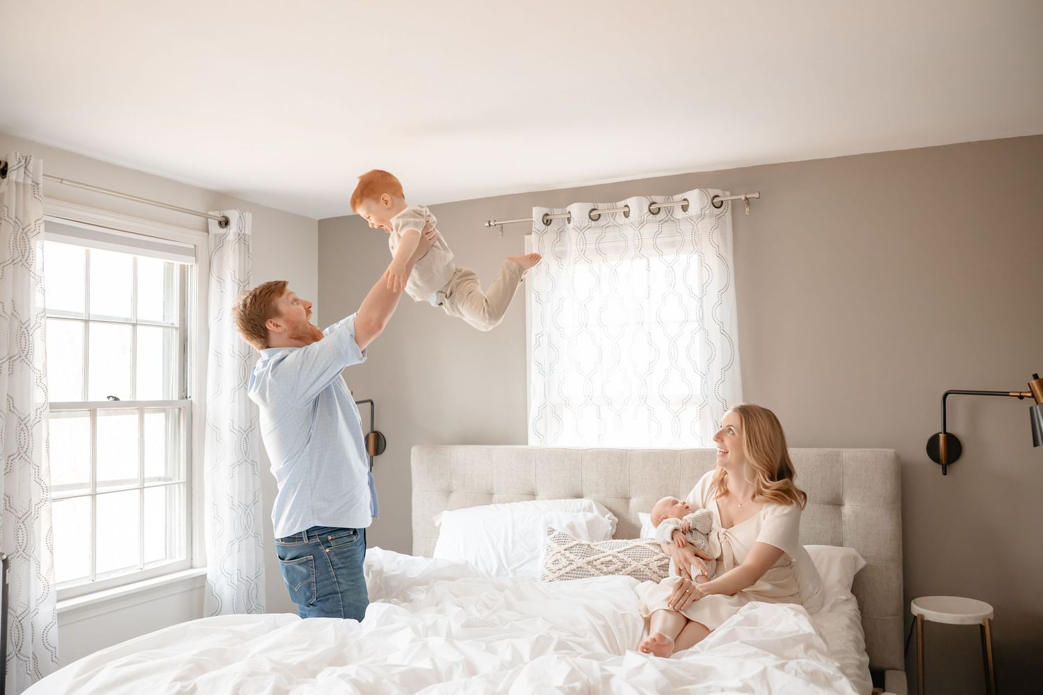A bright white bedroom scene with people playing and having fun with pillows during a pillow fight.