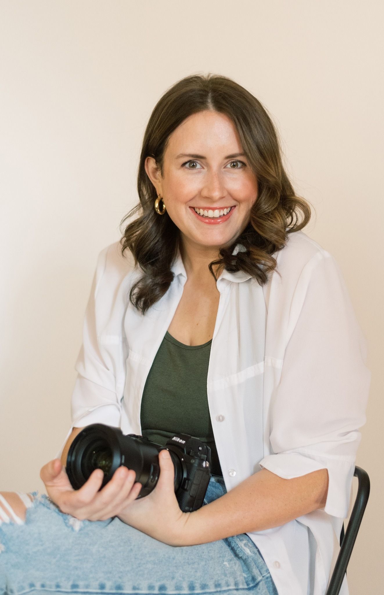Professional photographer in white blazer and olive top poses with camera against neutral background in four headshots.