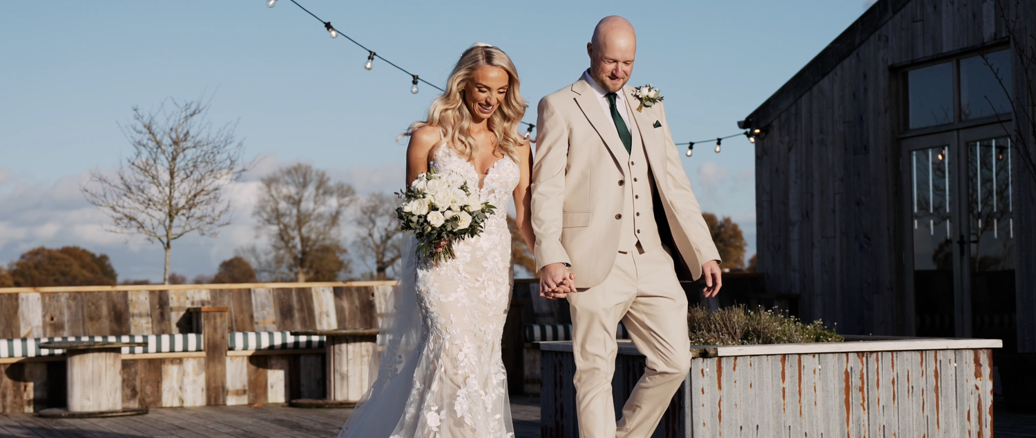 Rustic barn wedding venue with string lights and couple celebrating at sunset.