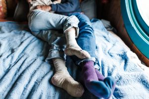 Close-up view of feet with colorful socks resting together on blue bedding.