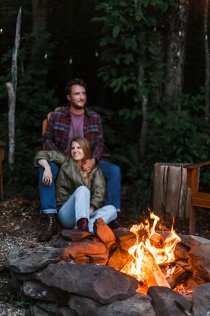 A cozy evening scene of people gathered around a glowing campfire with trees in the dark background.