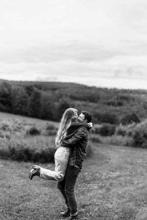 A romantic black and white photo of a couple embracing in a scenic mountain meadow.
