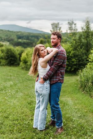 A couple shares a tender moment together in a lush green mountain field.
