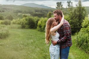 A romantic couple shares tender moments in a lush green meadow during a sunny summer day.