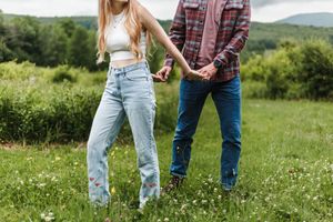 Two people holding hands while walking through a wildflower field on a cloudy day.