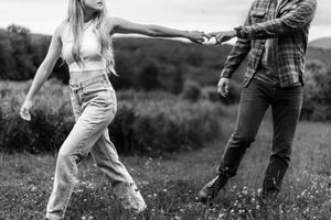 A couple spins and dances together in a grassy field on an overcast day.