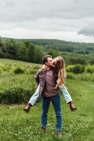 Playful couple performs a dip dance move in a summer meadow with mountains in the distance.