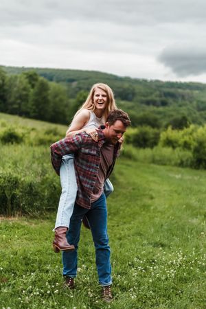 A playful sequence of two people embracing and laughing in a sunny meadow with wildflowers and green hills.
