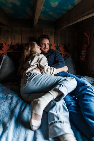 A couple cuddles together intimately on a couch in dim lighting.