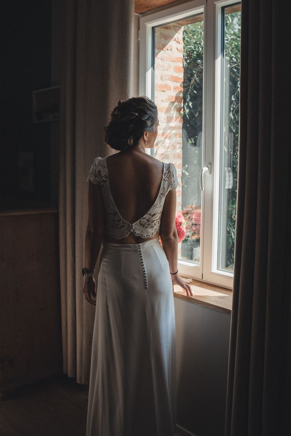 A wedding dress silhouette is illuminated by soft window light in a series of moody, romantic getting-ready photos.