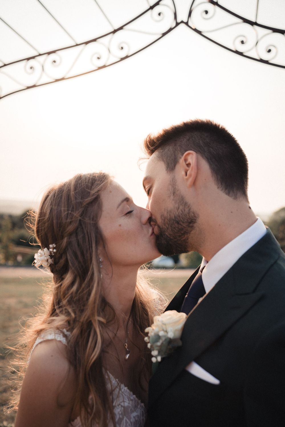 A romantic sunset wedding kiss between a couple in formal attire with soft golden light in the background.