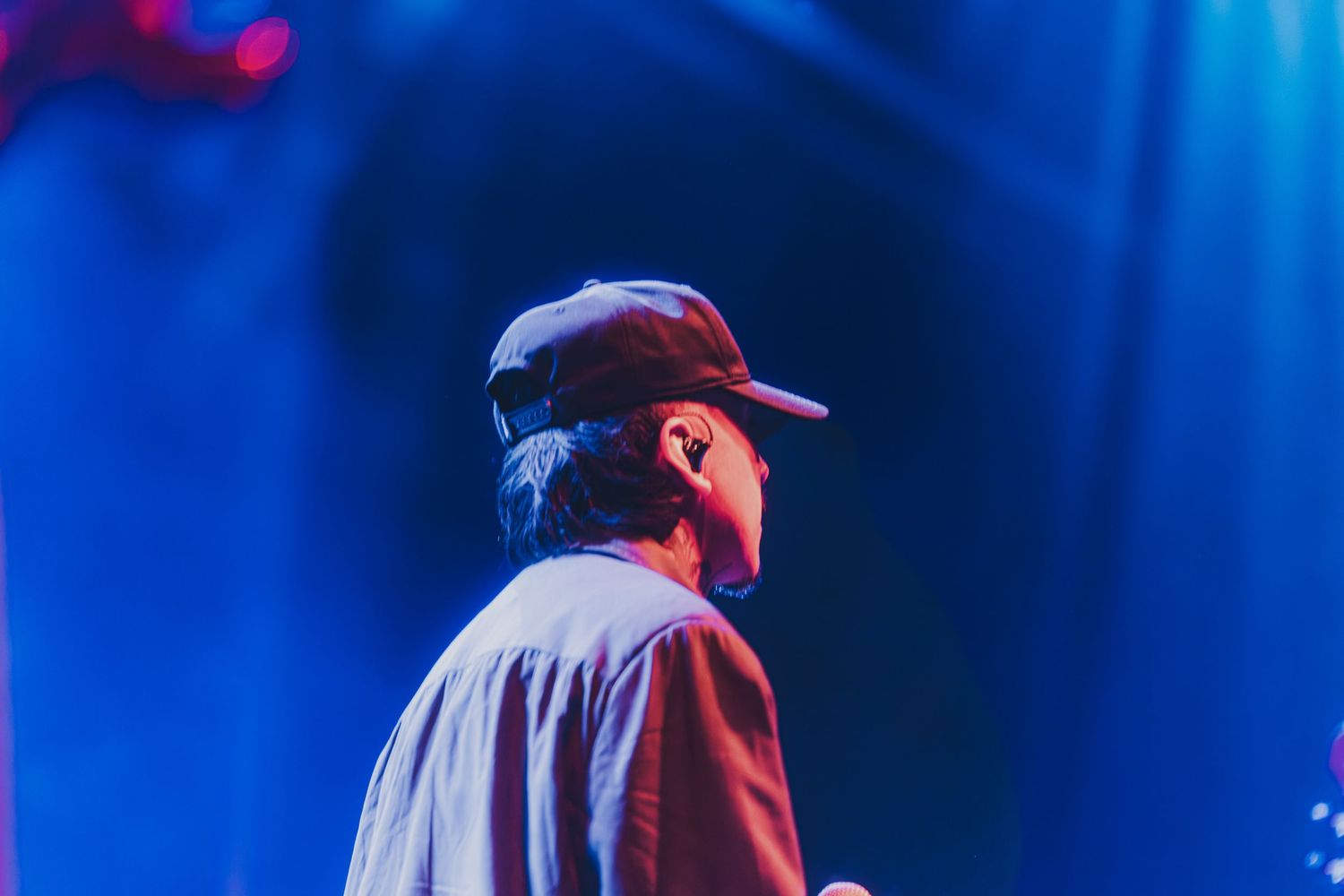 Musician performing on stage with dramatic blue lighting and red accents creating a moody atmosphere.