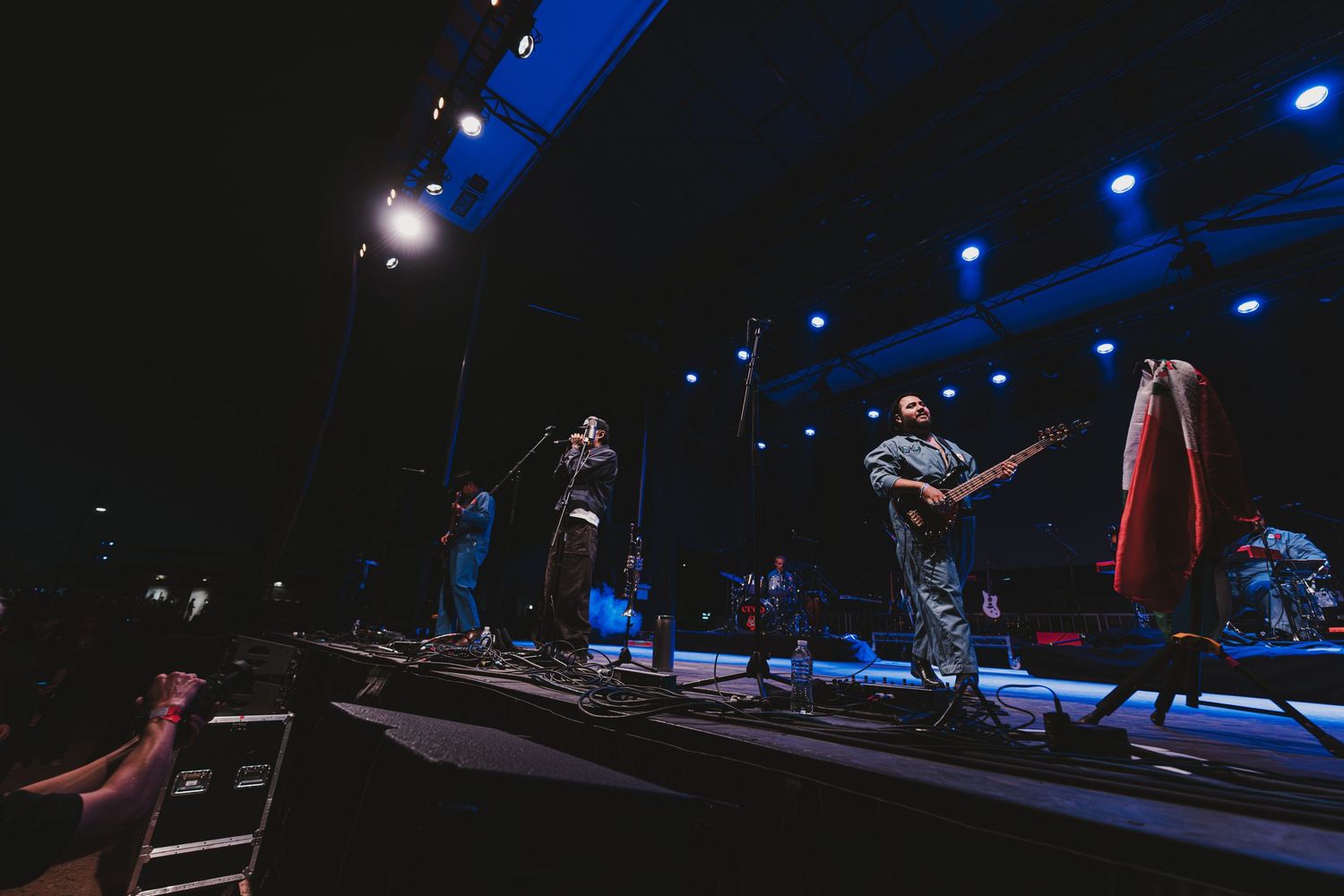 Musicians perform on a dark stage illuminated by blue spotlights during a live concert performance.