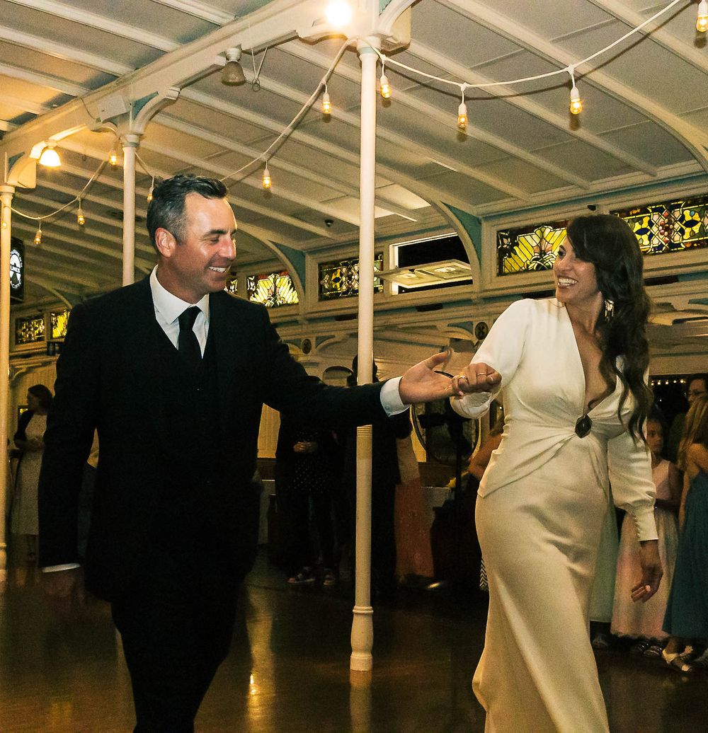 Guests dance and celebrate at an elegant indoor reception venue with string lights illuminating the white ceiling.