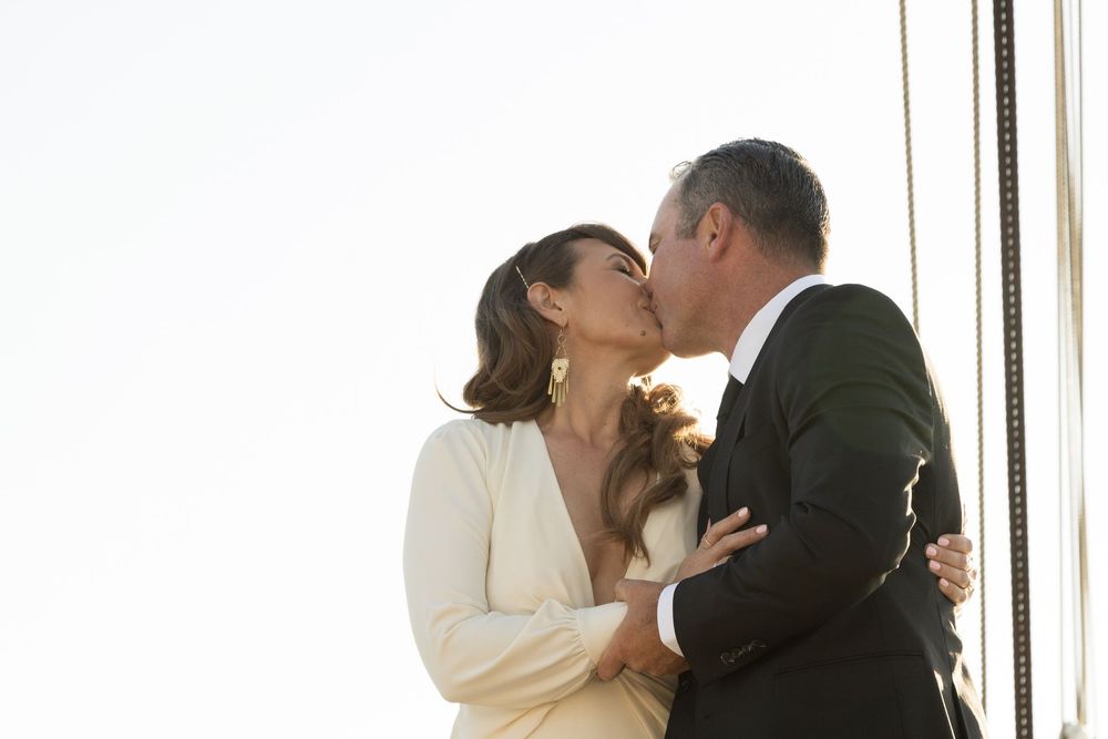 Three sequential wedding photos show a couple in formal attire sharing a romantic kiss in a bright interior setting.