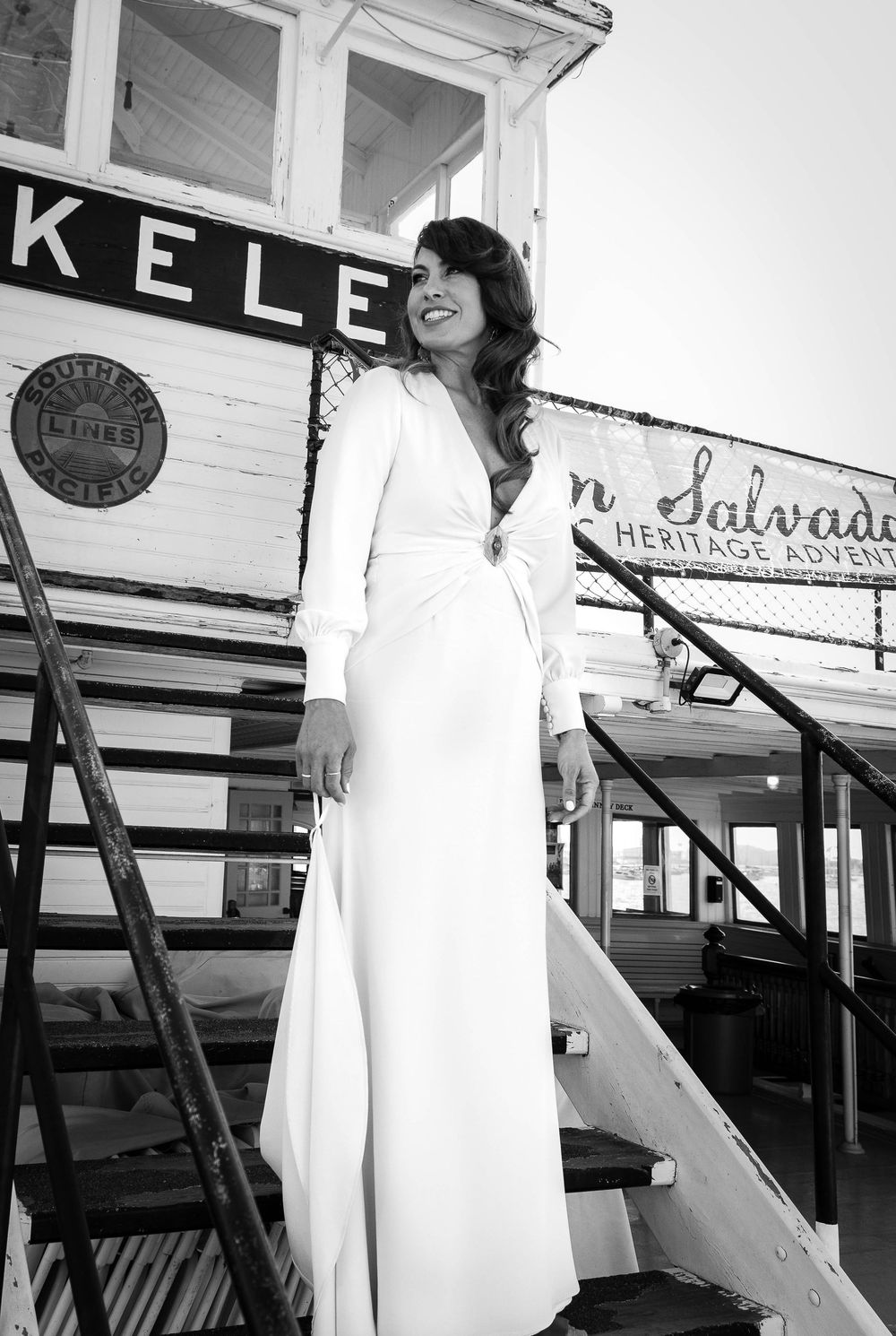 A black and white photograph showing a person in a white dress walking on a wooden boardwalk or deck.