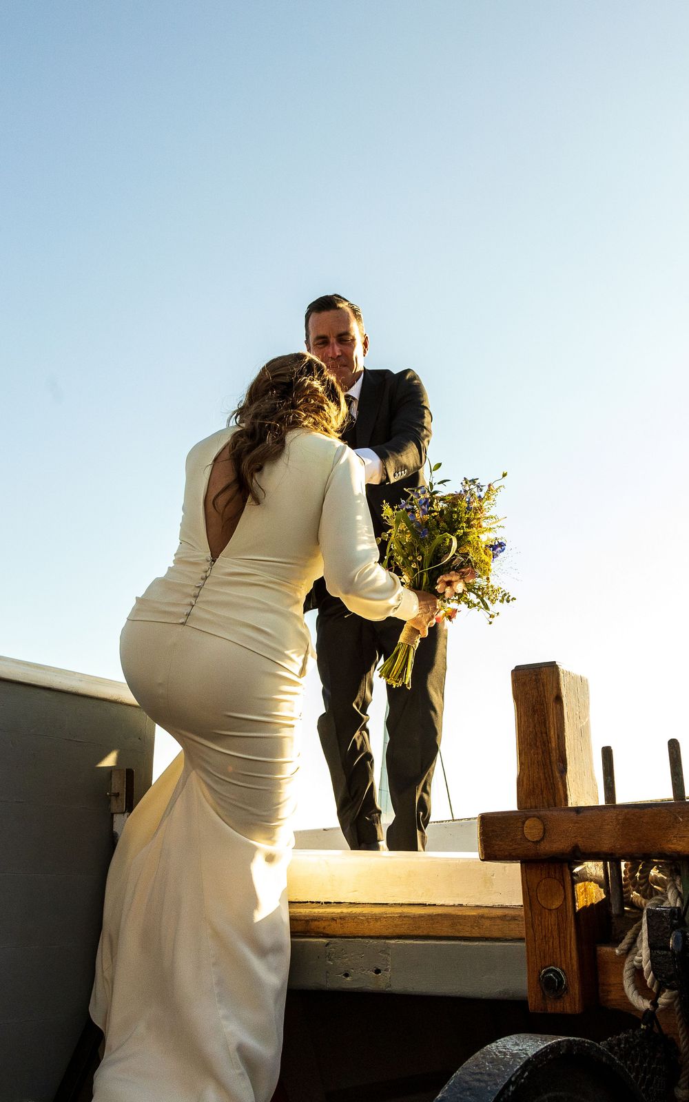 Newlywed couple shares romantic moment at sunset on rustic wooden dock with yellow bouquet.