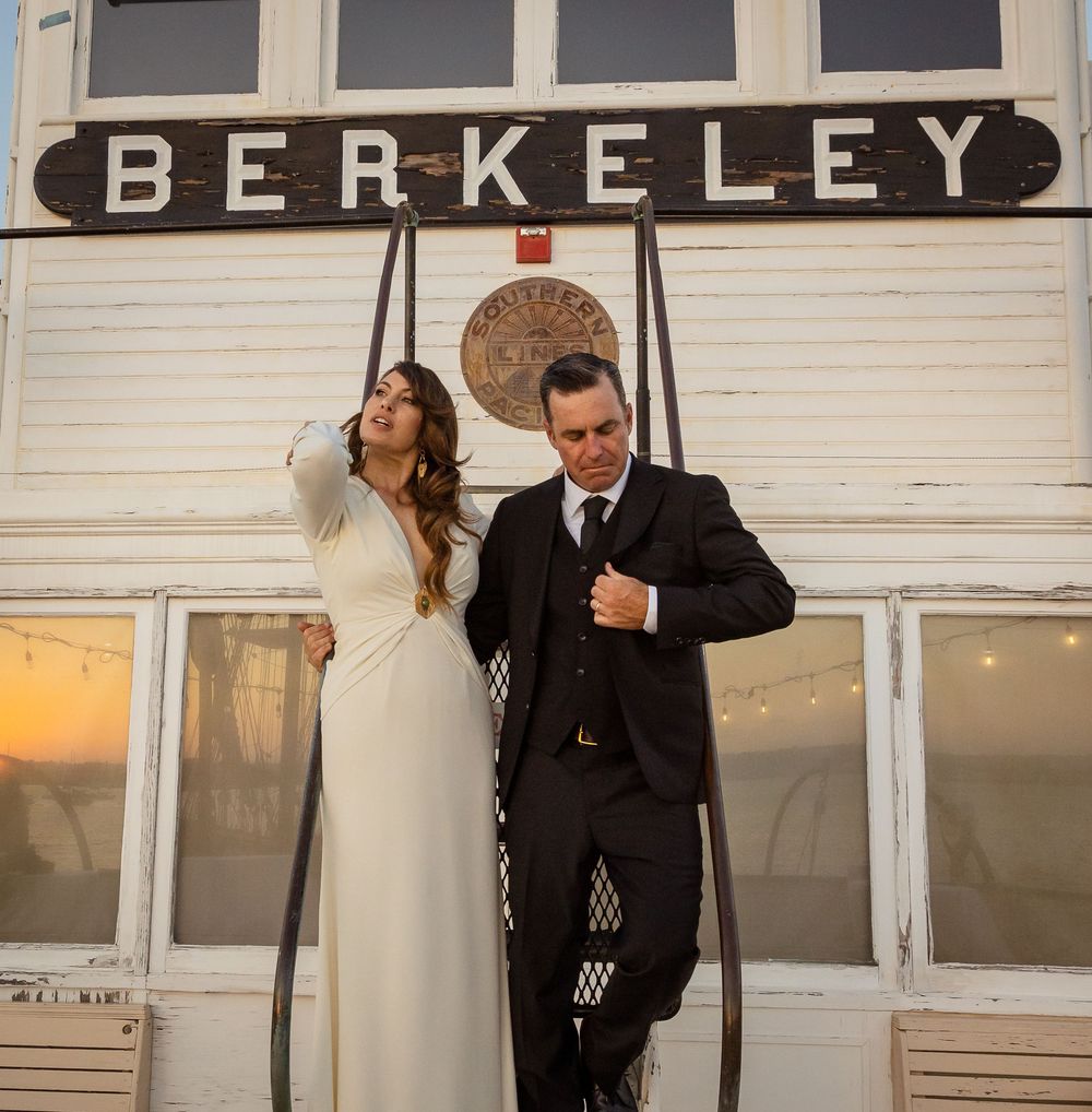 Couple in formal attire dancing together at a Berkeley venue with large windows visible in the background.