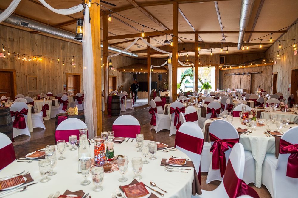 A wedding reception venue with elegant table settings featuring white linens, burgundy chair covers, and twinkling string lights.