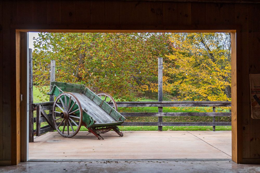 Rustic wooden barn door frames a scenic view of autumn trees and a historic cannon display in a park setting.